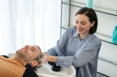 Erkek müşteri güzellik salonundaki sandalyede oturuyor ve saçlarını yıkatıyor.