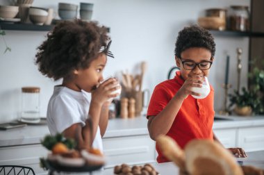 İki kardeş mutfakta kahvaltıda süt içiyor.