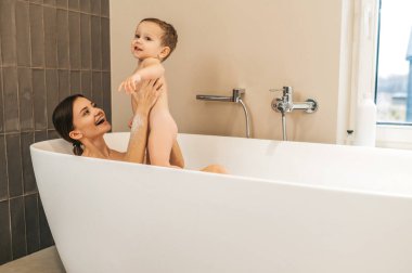 Neşeli genç kadın çocuğuyla banyo yapıyor.