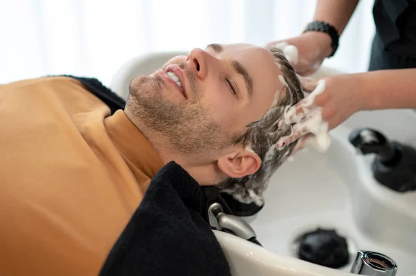 Young man sitting at the chait while having head massage and looking relaxed — Stock Photo, Image