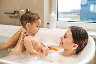 Gülümseyen kadın bebeğiyle banyo yapıyor.
