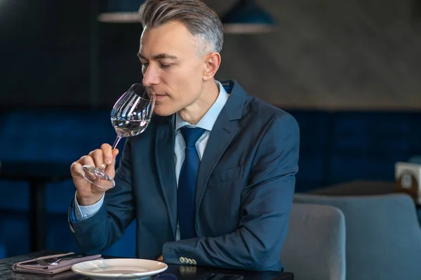 Ένας κομψός άντρας δοκιμάζει λευκό κρασί και δείχνει ευχαριστημένος. — Φωτογραφία Αρχείου