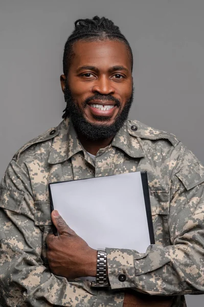 Sonriente joven soldado sosteniendo documentos en sus manos — Foto de Stock