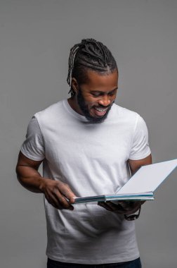 Neşeli erkek gri duvarın yanında duruyor ve bir şeyler okuyor.