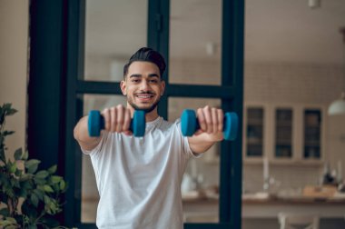 Dambılı bir adam evde antrenman yapıyor.