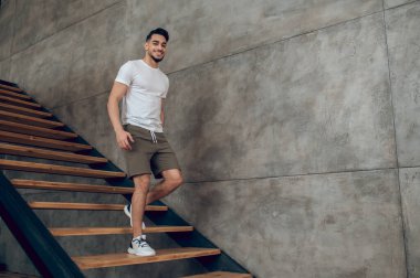 Evinin merdivenlerinde t-shirt ve şort giyen genç bir adam.