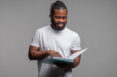 Odaklanmış memnun öğrenci duvarın yanında durup kitap okuyor.