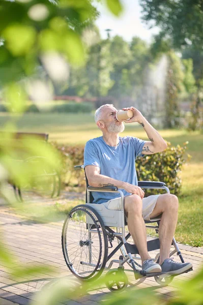 Un homme en fauteuil roulant assis dans le parc et prenant un café — Photo