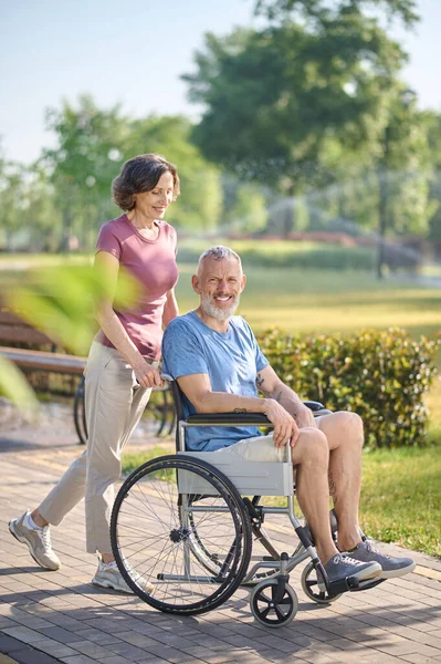 Une femme brune portant son mari en fauteuil roulant — Photo