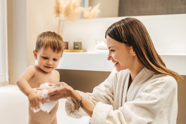 Lycklig mamma leker med sitt barn i badrummet — Stockfoto