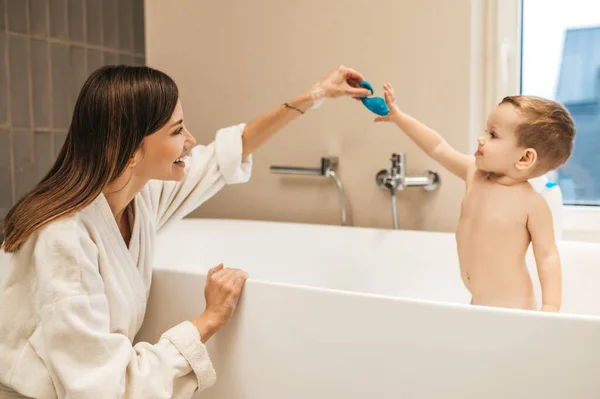 Весела жінка-батько грає зі своєю дитиною у ванній — стокове фото