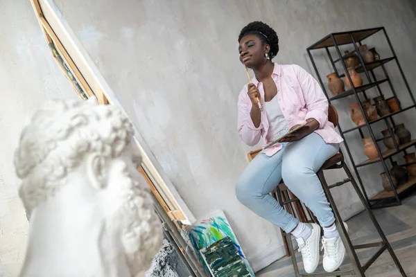 Зажатый африканский художник в розовой одежде выглядит вдохновлённым — стоковое фото