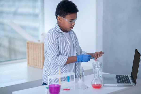 Un garçon brun en blouse de laboratoire a l'air occupé en faisant des expériences chimiques — Photo