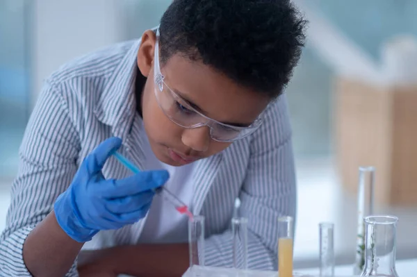 Un garçon brun en blouse de laboratoire tenant une seringue avec un réactif et ayant l'air occupé — Photo