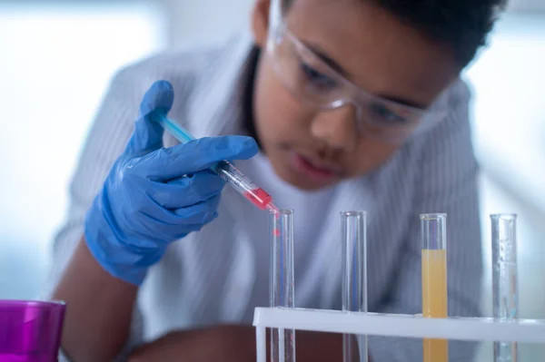 Un garçon brun en blouse de laboratoire tenant une seringue avec un réactif et ayant l'air occupé — Photo