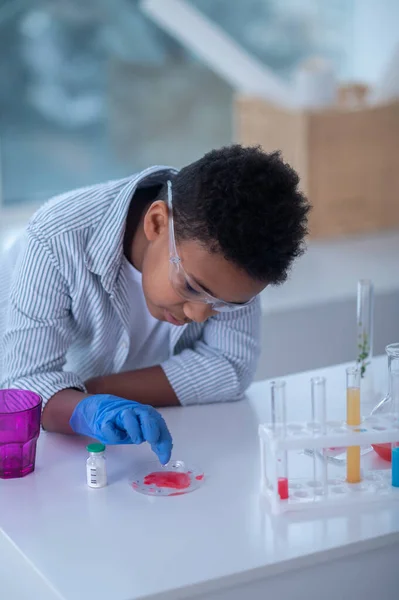 Un garçon en blouse de laboratoire travaillant avec des éprouvettes et regardant impliqué — Photo