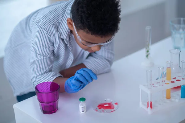 Un garçon en blouse de laboratoire travaillant avec des éprouvettes et regardant impliqué — Photo