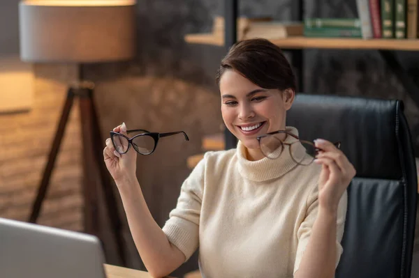 Una joven sosteniendo dos pares de anteojos y sonriendo — Foto de Stock