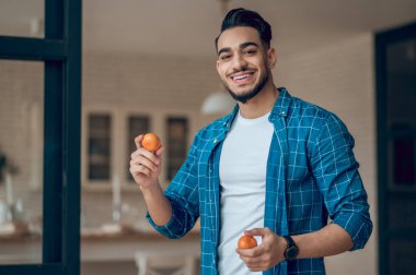 Mavi tişörtlü genç adam mandalinalarla hokkabazlık yapıyor.