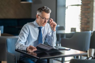 Orta yaşlı, şık elbiseli bir adam bir kafede masada oturuyor.