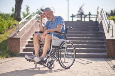Dışarıda tekerlekli sandalyede sakat bir adam düşünceli görünüyor.