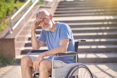 Dışarıda tekerlekli sandalyede sakat bir adam düşünceli görünüyor.