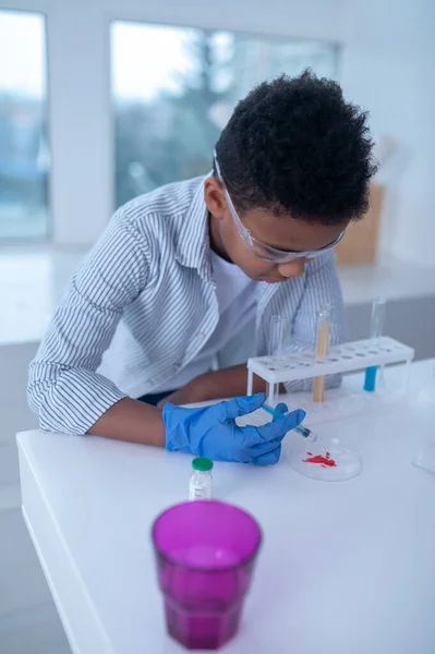 Un garçon brun en blouse de laboratoire a l'air occupé en faisant des expériences chimiques — Photo