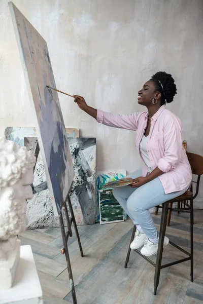 Una donna dalla pelle scura seduta vicino al cavalletto e alla pittura — Foto Stock