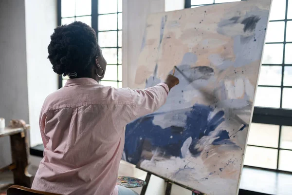 Una donna dalla pelle scura seduta vicino al cavalletto e alla pittura — Foto Stock