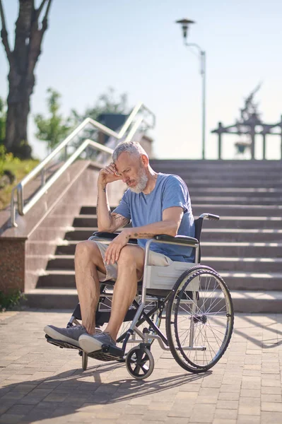 Un hombre discapacitado en una silla de ruedas al aire libre mirando reflexivo — Foto de Stock
