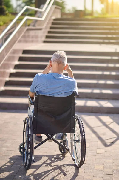 Tekerlekli sandalyede oturan bir adam arka tarafta dışarıda merdivenlerde oturuyor. — Stok fotoğraf