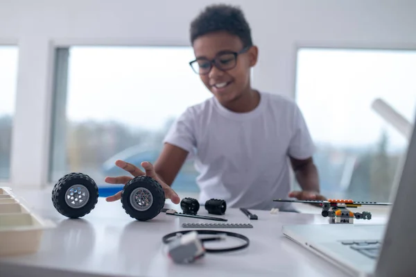 Um adolescente bonito sentado à mesa e brincando com rodas de brinquedo — Fotografia de Stock