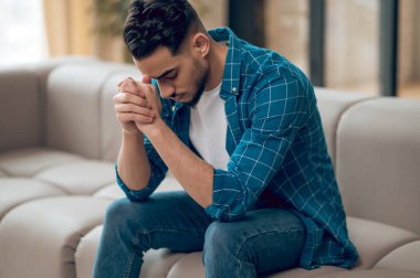 Genç, siyah saçlı, mutsuz bir bakışla oturan adam.