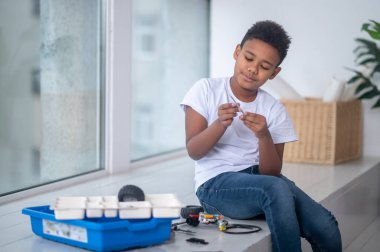 Koyu tenli bir çocuk pencerenin yanında bir oyuncakla oynuyor.