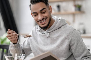 Genç bir adam kahvaltı yapıyor ve gazete okuyor.