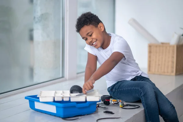 En mörkhyad pojke leker med en leksak nära fönstret. — Stockfoto