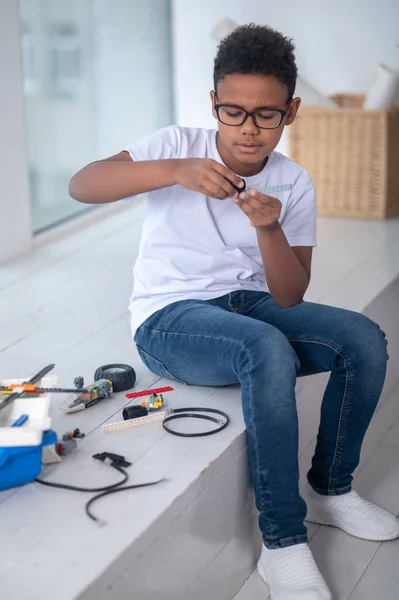 A dark-skinned boy in white tshirt and jeans playing with a toy transformer — ストック写真