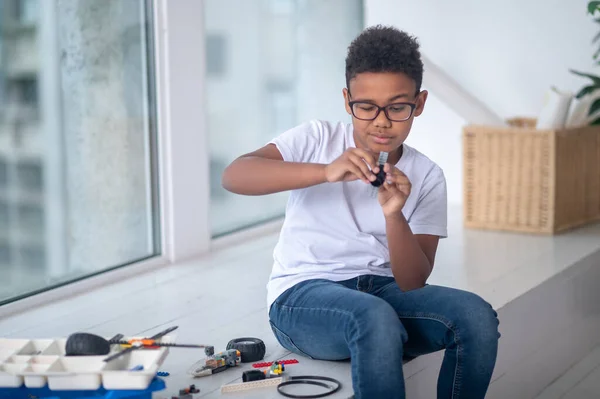 En mörkhyad pojke i vit tröja och jeans som leker med en leksakstransformator — Stockfoto