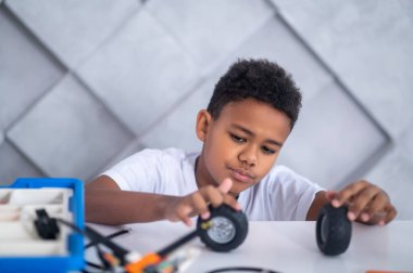 Oyuncak araç tekerleriyle oynayan esmer tenli bir çocuk.