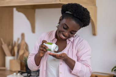 Genç Afrikalı kadın vitamin alıyor ve gülümsüyor.