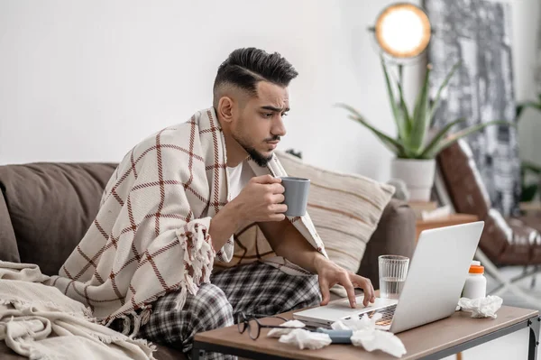 A sick man sitting at the laptop and talking to the doctor online — Foto de Stock