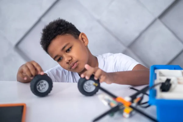 Ein dunkelhäutiger Junge spielt mit Rädern eines Spielzeugs — Stockfoto