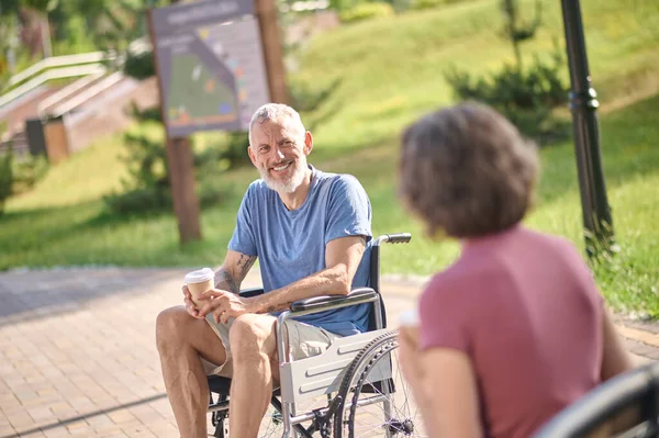 Un homme en fauteuil roulant et une femme prenant un café dans le parc — Photo