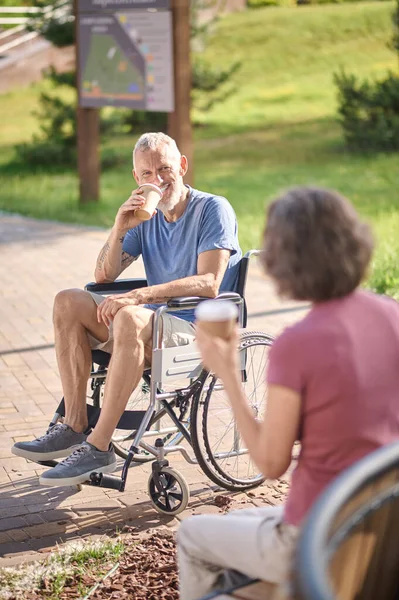 Un homme en fauteuil roulant et une femme prenant un café dans le parc — Photo