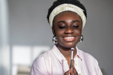 Açık renk elbiseli, rimel tutan Afrikalı bir kadın.