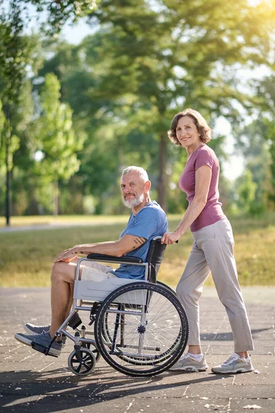 Une femme portant son mari en fauteuil roulant dans un parc — Photo
