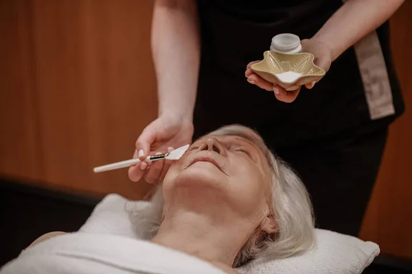 Kosmetolog nakładający maskę rewitalizującą na twarz kobiety — Zdjęcie stockowe