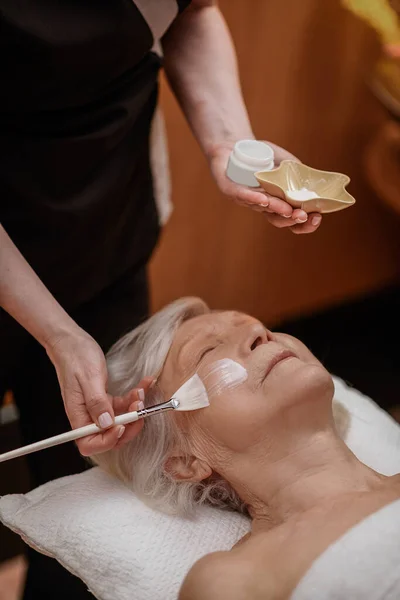 Kosmetolog nakładający maskę rewitalizującą na twarz kobiety — Zdjęcie stockowe