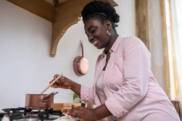 Spokojený africký žena v růžové oblečení vaření v kuchyni — Stock fotografie