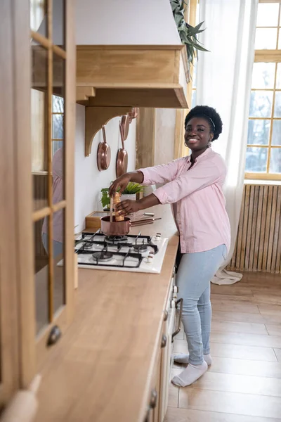 Artı, mutfakta yemek pişiren pembe elbiseli Afrikalı kadın.